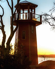 A lookout tower shaped like a lighthouse, shines in the sunset sitting on a property above Grand Lake.